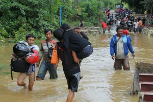 GENDONG KELUARGA. Gara-gara jembatan penghubung Desa Raja dan Desa Munggu, Kecamatan Ngabang, Kabupaten Landak, terendam air, pria ini menggendong keluarganya untuk sampai ke seberang, Sabtu (19/12). ANTONIUS