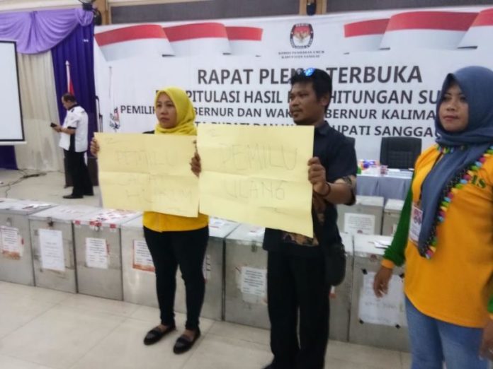 PROTES. Dua pendukung pasangan YAS membentengkan poster bertuliskan Pilkada ulang dan Pilkada cacat hukum di ruang rapat pleno, Jumat (6/7). Warga for RK