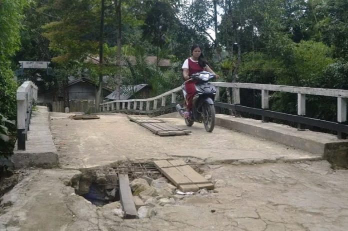 Jembatan Berlubang. Warga berkendara melalui jembatan Sungai Boli yang kondisi lantainya sudah berlubang serta mengancam keselamatan warga yang melintas. Warga for Rakyat Kalbar